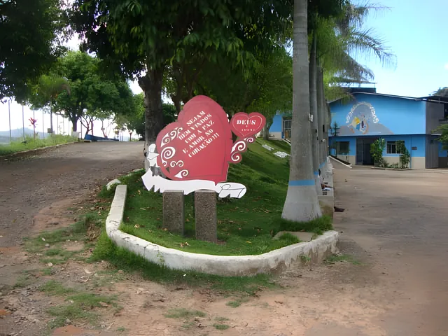 Foto real: coração vermelho de boas-vindas na entrada da Colônia, com o prédio azul ao fundo